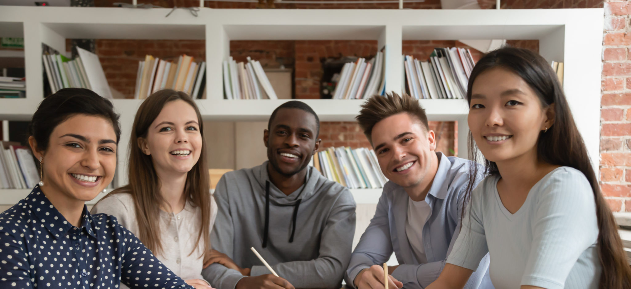Happy mixed race students gathered in classroom, looking at camera